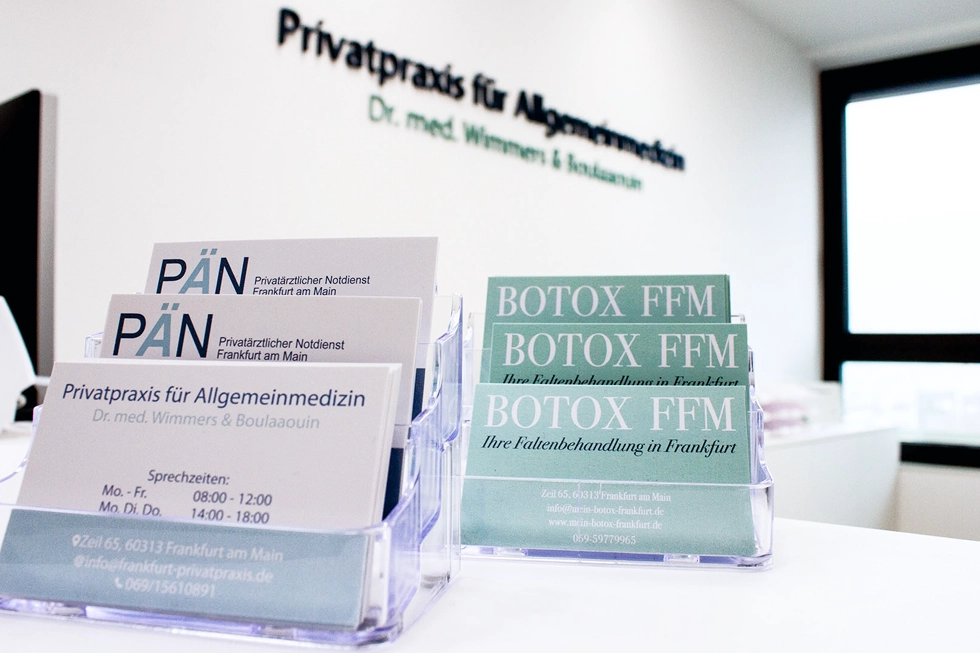 Empfangstheke einer modernen Arztpraxis mit Visitenkarten und Botox-Flyern.