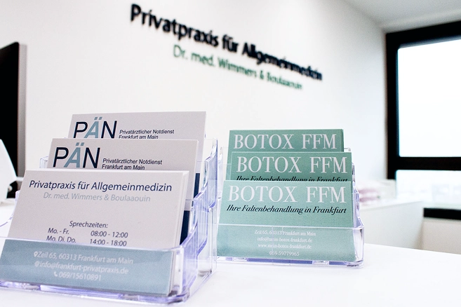 Empfangstheke einer modernen Arztpraxis mit Visitenkarten und Botox-Flyern.